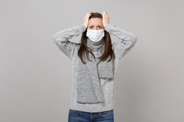 Young woman in gray sweater, scarf with sterile face mask put hands on head isolated on grey background in studio. Healthy lifestyle ill sick disease treatment cold season concept. Mock up copy space.