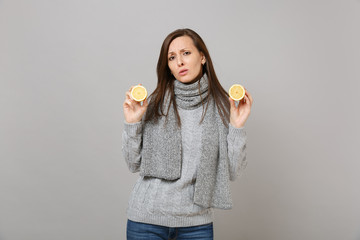 Wall Mural - Tired sad young woman in gray sweater, scarf hold lemons isolated on grey wall background, studio portrait. Healthy fashion lifestyle, people sincere emotions, cold season concept. Mock up copy space.