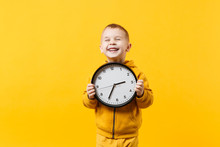 Little Kid Boy 3-4 Years Old Wearing Yellow Clothes Hold Clock Isolated On Orange Wall Background, Children Studio Portrait. People Sincere Emotions, Childhood Lifestyle Concept. Mock Up Copy Space.