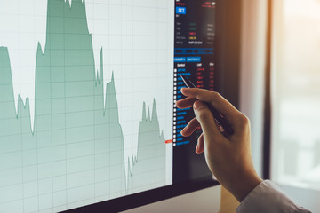 Close up of businessman hand pointing to stock market chart and analysis on computer screen.