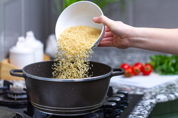 Cooking dry golden yellow long rice in a saucepan for delicious meals from groats with vegetables at home