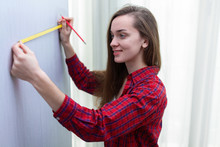 Young Attractive Woman In T-shirt Is Engaging In Home Repairs And Measuring The Length Of The Wall By Tape Measure