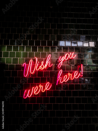 Fotografía 80's styled red neon text Wish you were here on a black tiles wall background