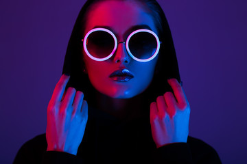 portrait of fashion young girl in a black sweater with a hood and round sunglasses in red and blue n