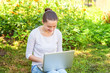 © Юлия Завалишина - Freelance business concept. Young woman sitting on green grass lawn in city park working on laptop pc computer. Lifestyle authentic candid student girl studying outdoors. Mobile Office