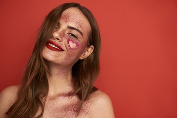 Wall Mural - Smiling naked young woman with creative makeup situating on red background