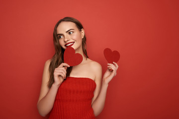 Wall Mural - Glamorous model keeping decorative hearts in arms on red background