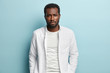 © WHstudio Leushin N - Image of sad sorrowful black man with thick bristle, wears white shirt, feels troublesome, looks at camera with miserable expression, isolated over blue background. People, melancholy, problem concept