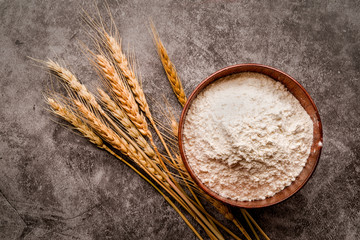 baking flour on dark background with wheat ears flat lay top view