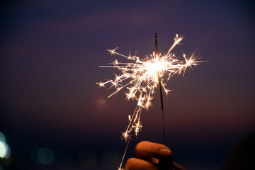 Wall Mural - Happy cute girl holding a sparkler on beach during sunset. Celebration concept.