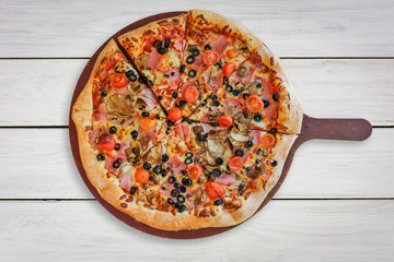 Top view of a traditional italian pizza with: ham,  mushrooms, cherry tomatoes, mozzarella, black olives on a wooden white table ( high details).