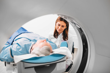 Radiographer reassuring senior man going into CT scanner in hospital