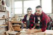 © alfa27 - Dad and his son dressed in checkered red shirts and wearing safety glasses are working in the carpentry workshop, son is learning to work with a saw under father s supervision.