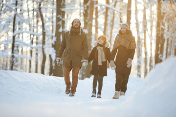 Wall Mural - Full length portrait of happy family holding hands enjoying walk in winter forest lit by sunlight, copy space