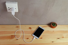 Plug In Power Outlet Adapter Cord Charger Of Mobile Phone On Wooden Floor
