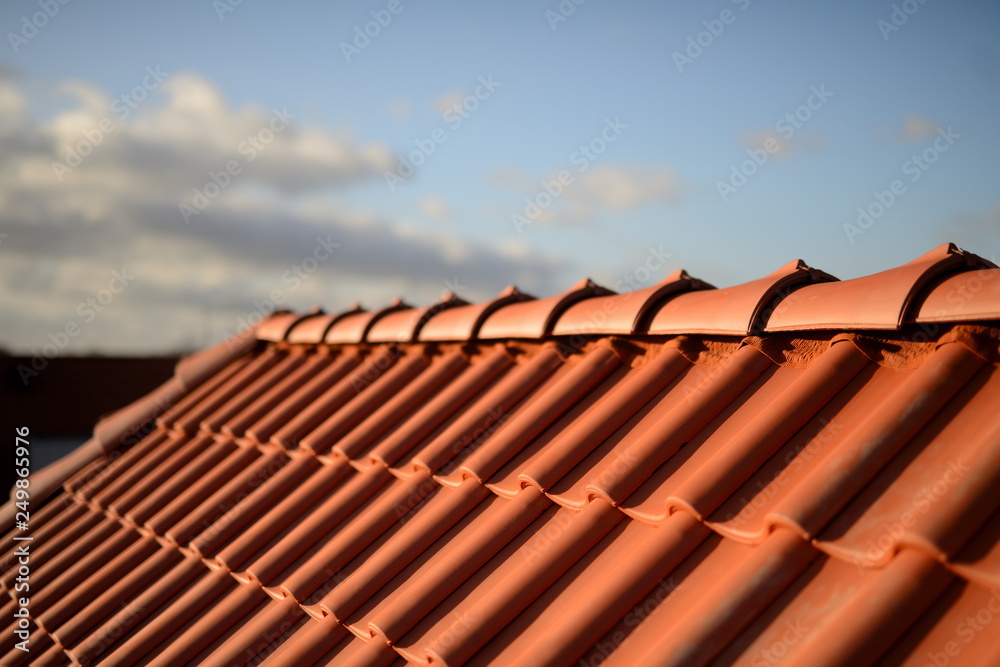 Dachfirst und glänzend rote Dachziegel Pfannen vom Dachdecker im Sonnenschein vor  dunklem Hintergrund - obrazy, fototapety, plakaty 