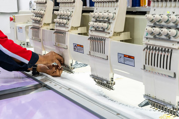 Operator or tailor working on modern and automatic high technology sewing machine for textile or clothing apparel making manufacturing process in industrial