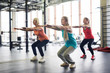 © Seventyfour - Group of mature active females squatting and stretching arms forwards during workout in fitness center