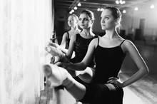 Three Young Cute Ballerinas Perform Exercises On A Choreographic Machine Or Barre On The Background Of A Ballet Class
