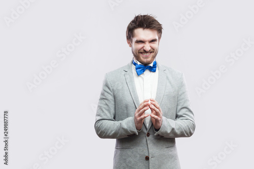 Cuadros en Lienzo Portrait of cunning handsome bearded man in casual grey suit and blue bow tie standing with funny face and palm hand looking at camera with idea