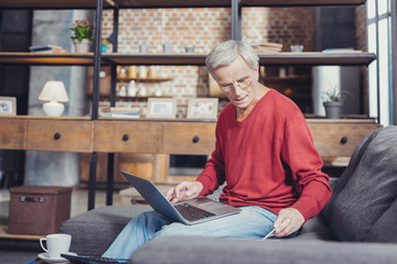 Wall Mural - Modern pensioner holding a laptop while sitting on the sofa