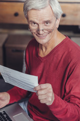 Wall Mural - Positive pensioner smiling while holding a bill and a laptop