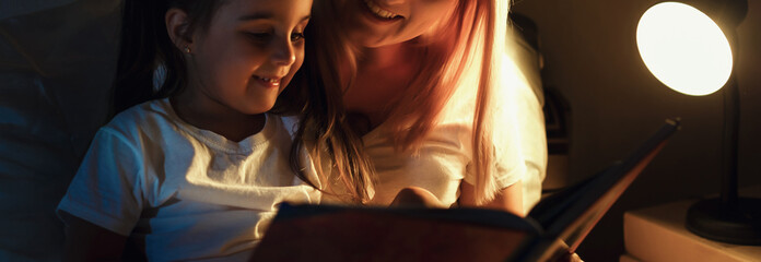 mother and child girl reading a book in bed before going to sleep