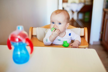 Wall Mural - Little baby girl sitting in high chair and drinking water from sippy cup