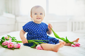 Wall Mural - Baby girl in blue dress playing with bunch of pink tulips