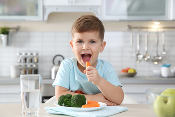 Canvas Print - Adorable little boy eating vegetables at table in kitchen