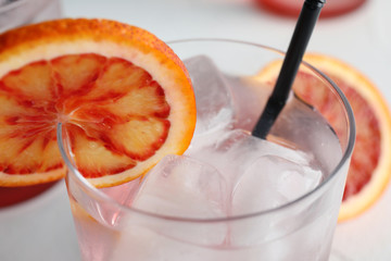 Glass of drink with ice cubes and orange, closeup