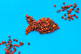 Fototapeta Tulipany - Cat food. Dry food in shape of fish on blue backgorund top view copy space