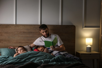 Poster - Young father reading book for his children in bed