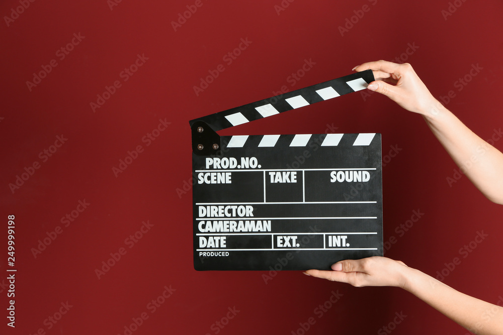 Female hands with cinema clapperboard on color background