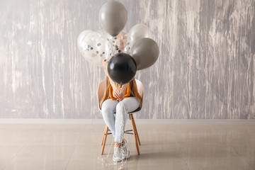 Wall Mural - Beautiful young woman with balloons sitting on chair against grunge wall