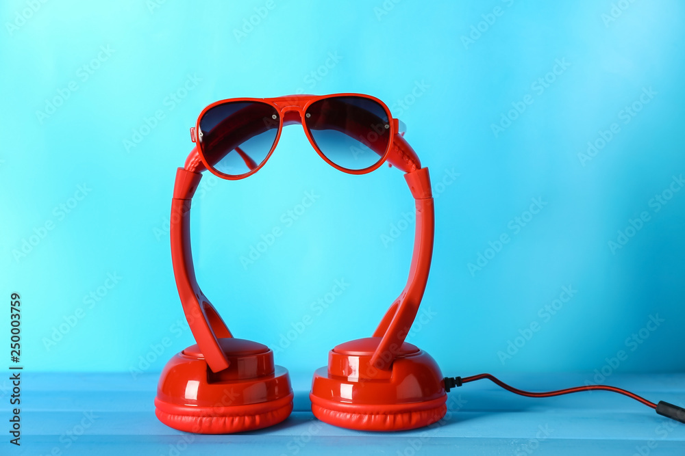 Modern headphones and sunglasses on color background