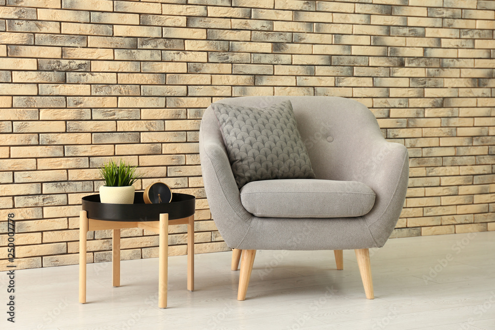 Comfortable armchair and table near brick wall