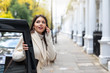 Attraktive Geschäftsfrau mit Handy in der Hand steigt aus einem schwarzen Taxi in London 