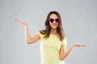 summer, valentine's day and people concept - smiling young woman or teenage girl in heart-shaped sunglasses holding something on palms over grey background