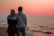 Young Couple Standing And Staring At Small Waves Of Sea And Pink Sunset Light. Peaceful Atmosphere In Summer Evening. Back View. Empty Place For Romantic Text, Quote Or Sayings On Nature Background.