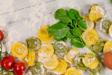 Wall Mural - Homemade fresh Italian ravioli pasta on white wood table  with flour, basil, tomatoes,background,top view.