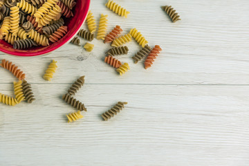 Wall Mural - Raw uncooked three-colored Fusilli  in a red bowl on white wood table.