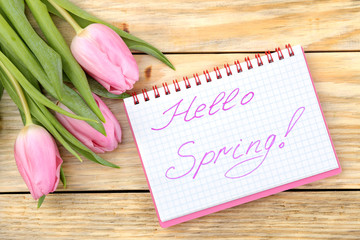  Beautiful bouquet of pink tulips flowers and text hello spring in notebook on natural wooden background. view from above. Spring. holidays.