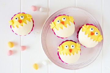 Poster - Hatching spring chick cupcakes on a white plate. Flay lay against a white wood background.