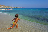 Fototapeta Łazienka - A three and a half years old girl playing small shells in the sea at Kalafatis Beach in Mykonos