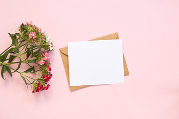 Top view of envelope and blank greeting card with flowers on pink background.