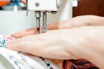 Sticker - Sewing on a sewing machine. Woman uses a sewing machine to sew clothes, decorations from material. Fashion and beauty concept, sewing clothes. A woman works at home, passion.