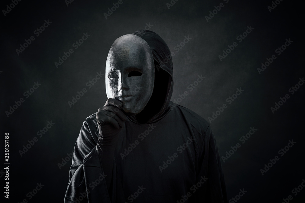Scary figure in hooded cloak with mask in hand  - obrazy, fototapety, plakaty 