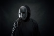 Scary figure in hooded cloak with mask in hand 