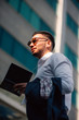 © qunica.com - Confident businessman is in urban neighborhood with his headphones on, holding a pen and holding his notebook.